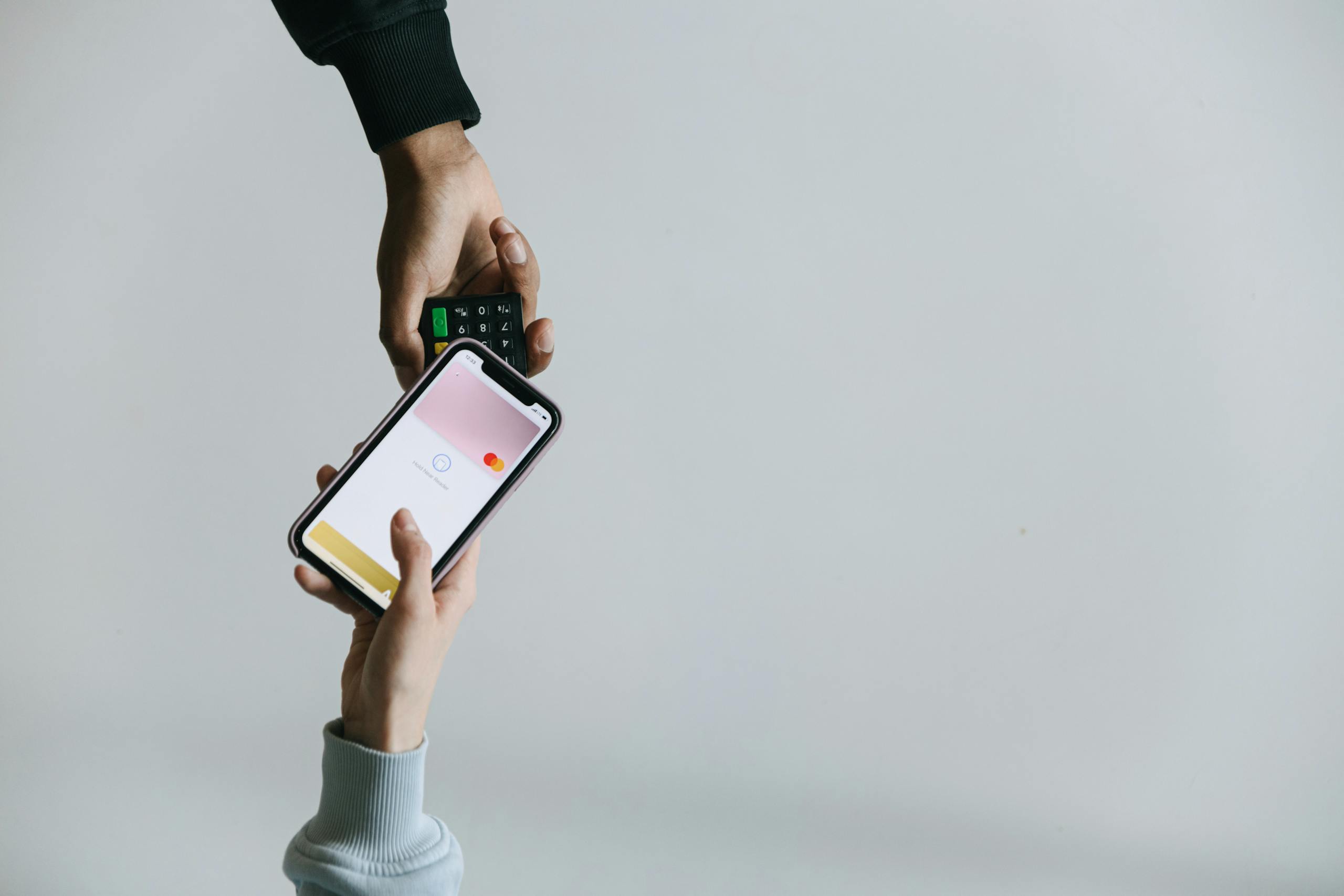 Hands using smartphone and terminal for cashless payment, showcasing modern transaction methods.