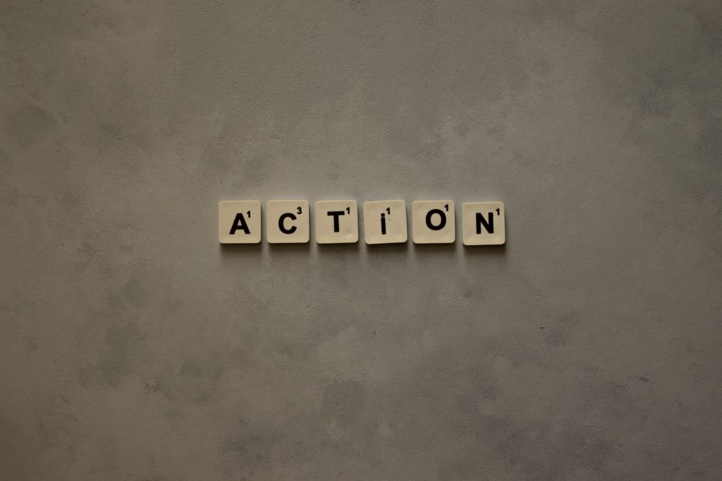 Scrabble tiles forming the word 'Action' on a textured gray surface, conveying motivation.