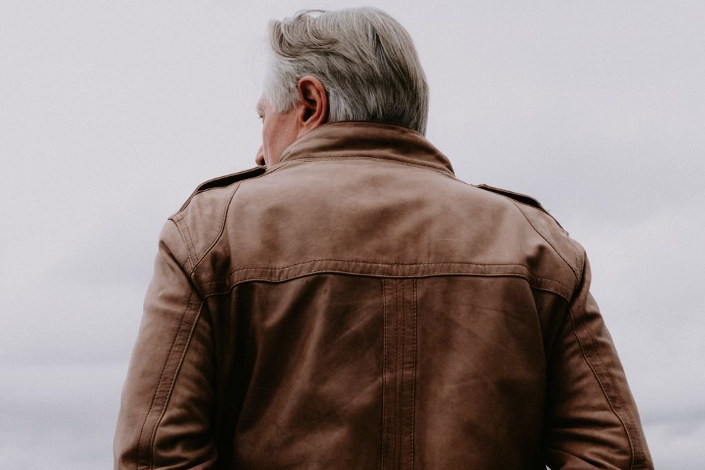 Stylish man in a brown leather jacket facing away, showcasing fashion and design.