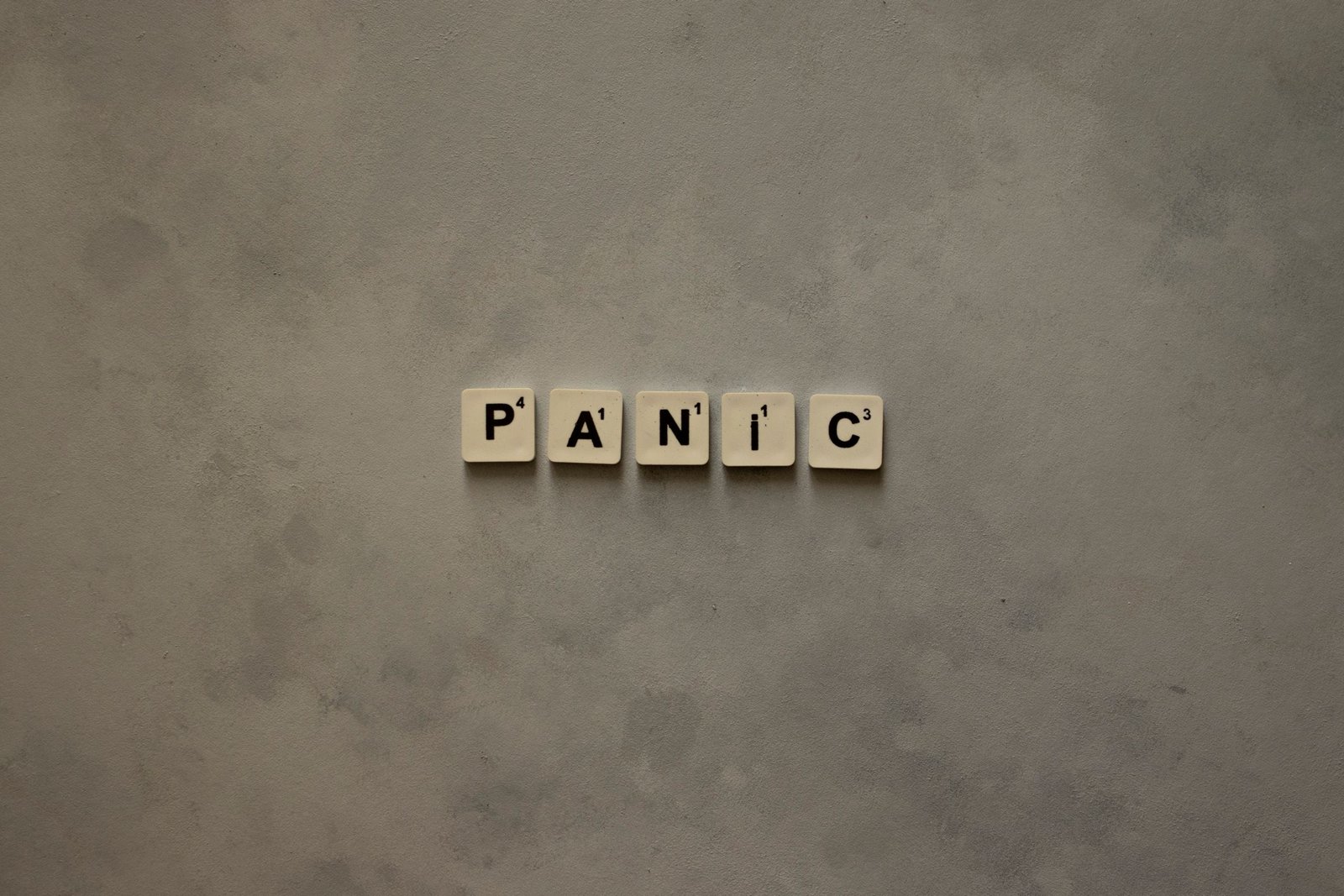 Scrabble tiles forming the word 'Panic' on a simple neutral background, symbolizing anxiety.