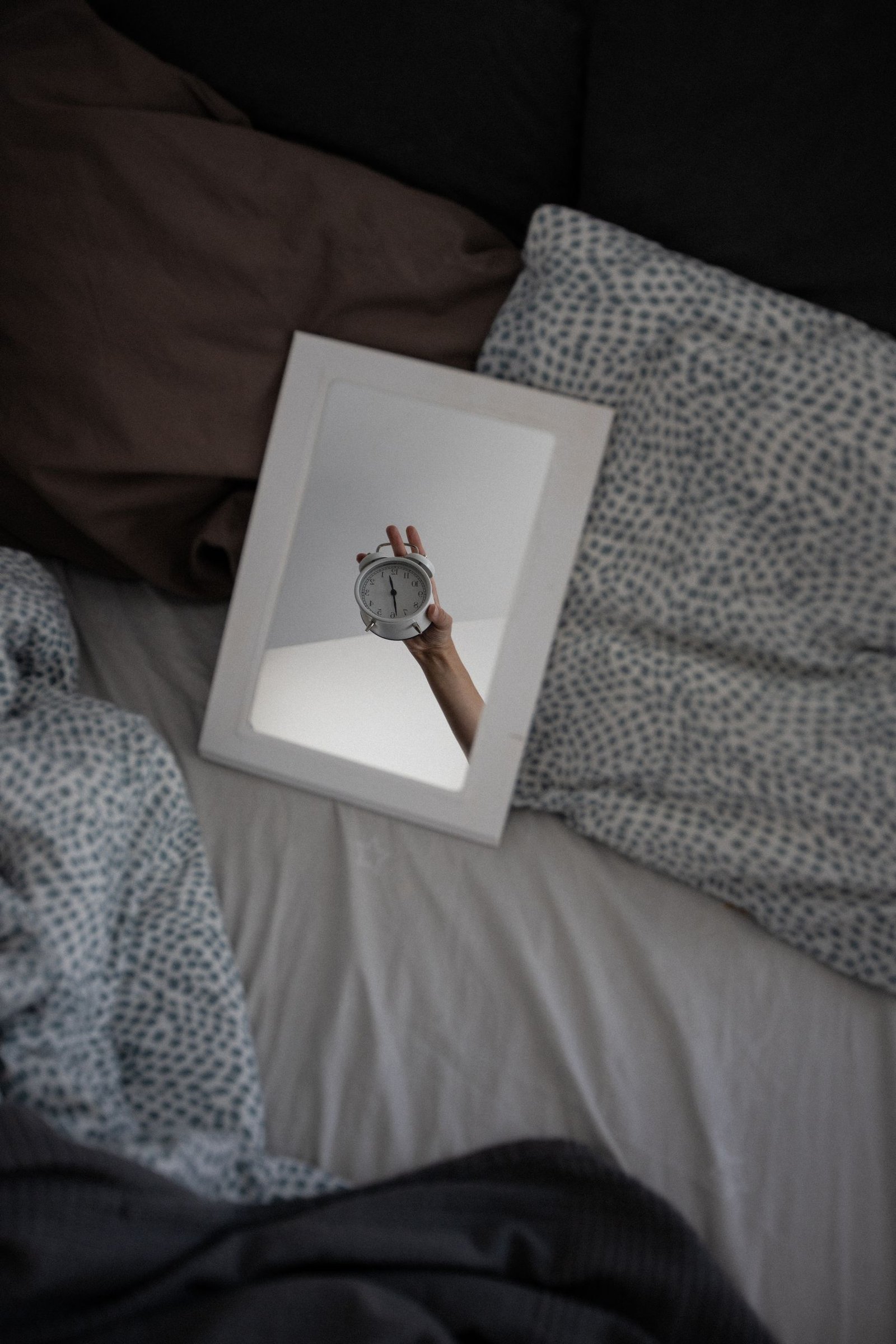 Unique reflection of an alarm clock in a mirror on a cozy bed setting.
